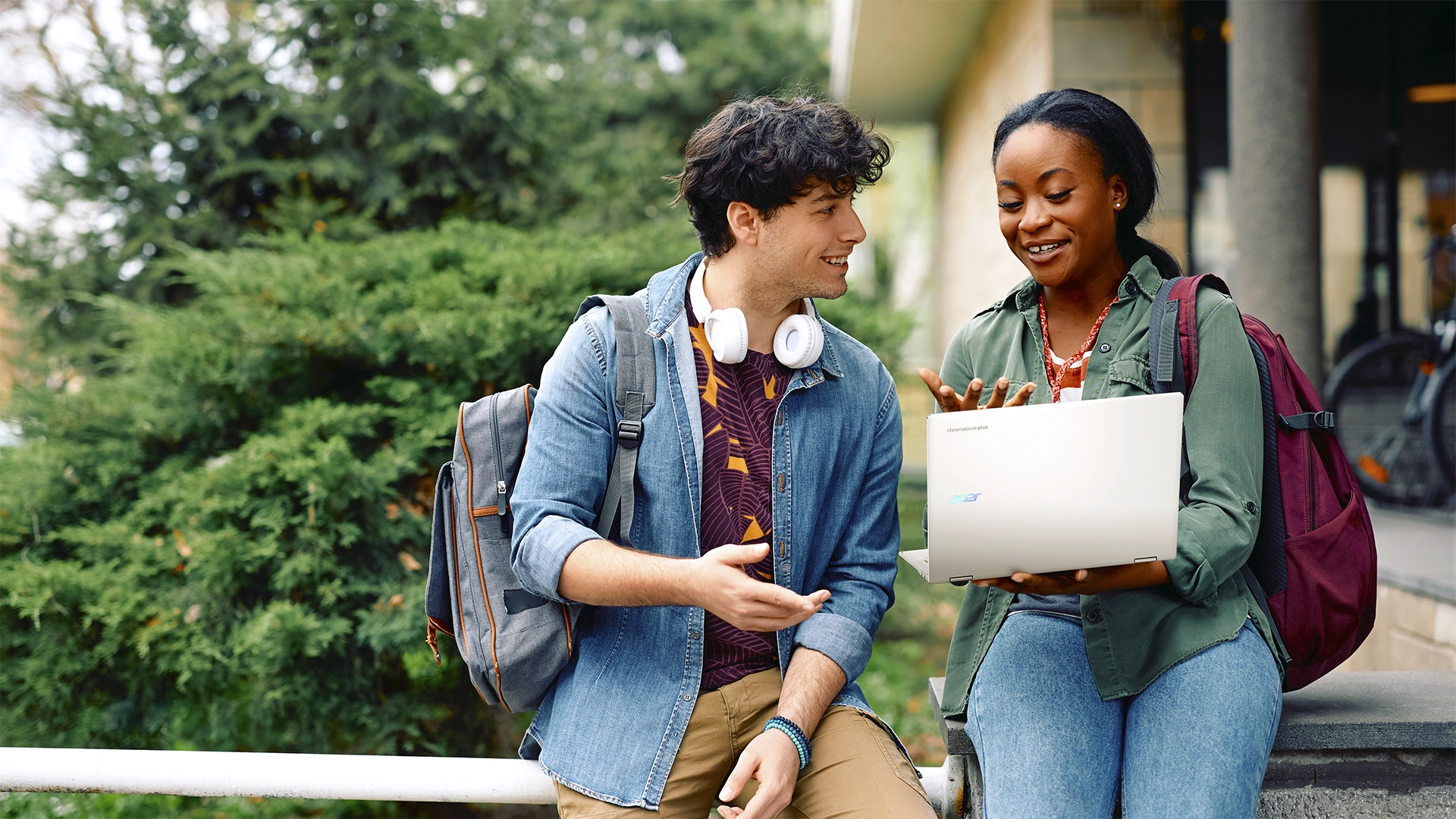 Zwei junge Erwachsene unterhalten sich im Freien, eine hält einen Acer Laptop in den Händen.