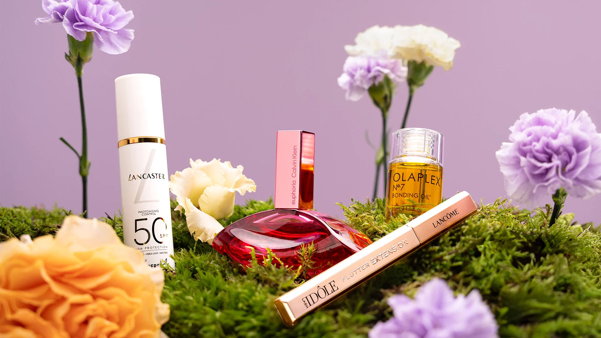 Kosmetik- und Duftprodukte auf grünem Moos, umgeben von Blumen. Produkte von Lancaster, Calvin Klein, Olaplex und Lancôme.